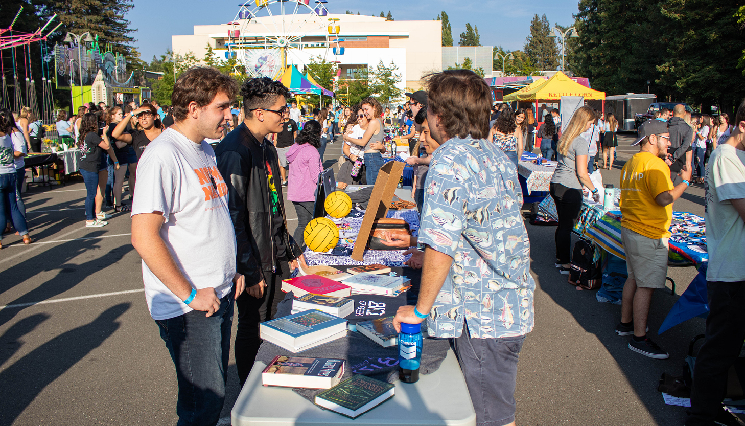 Students talking across a table at a large event with a ferris wheel in background