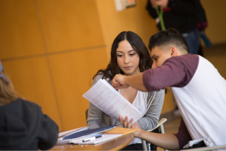 Student in classroom talking to another student and looking at a piece of paper