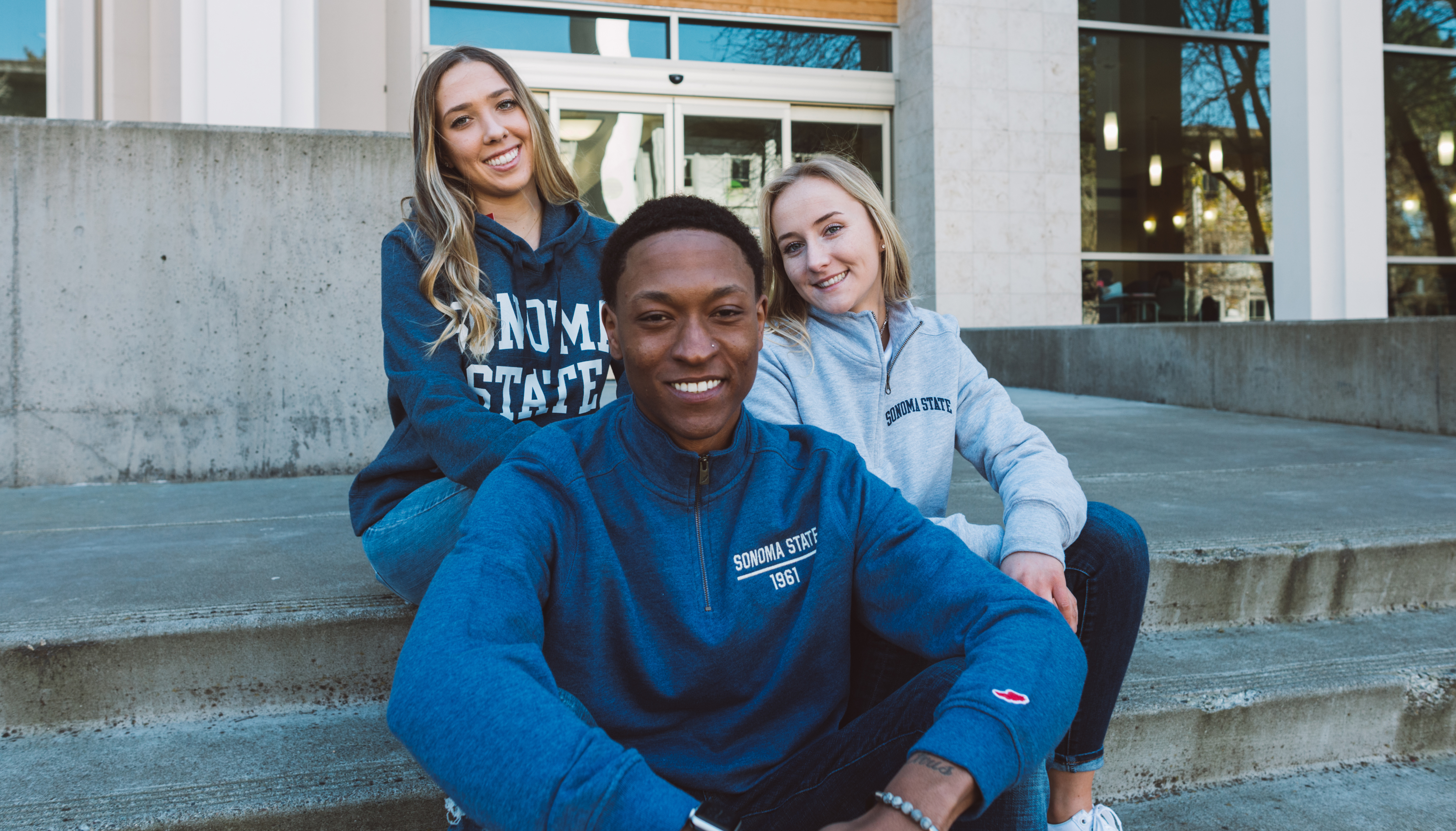 Three students in SSU gear sitting on steps outsidecampus