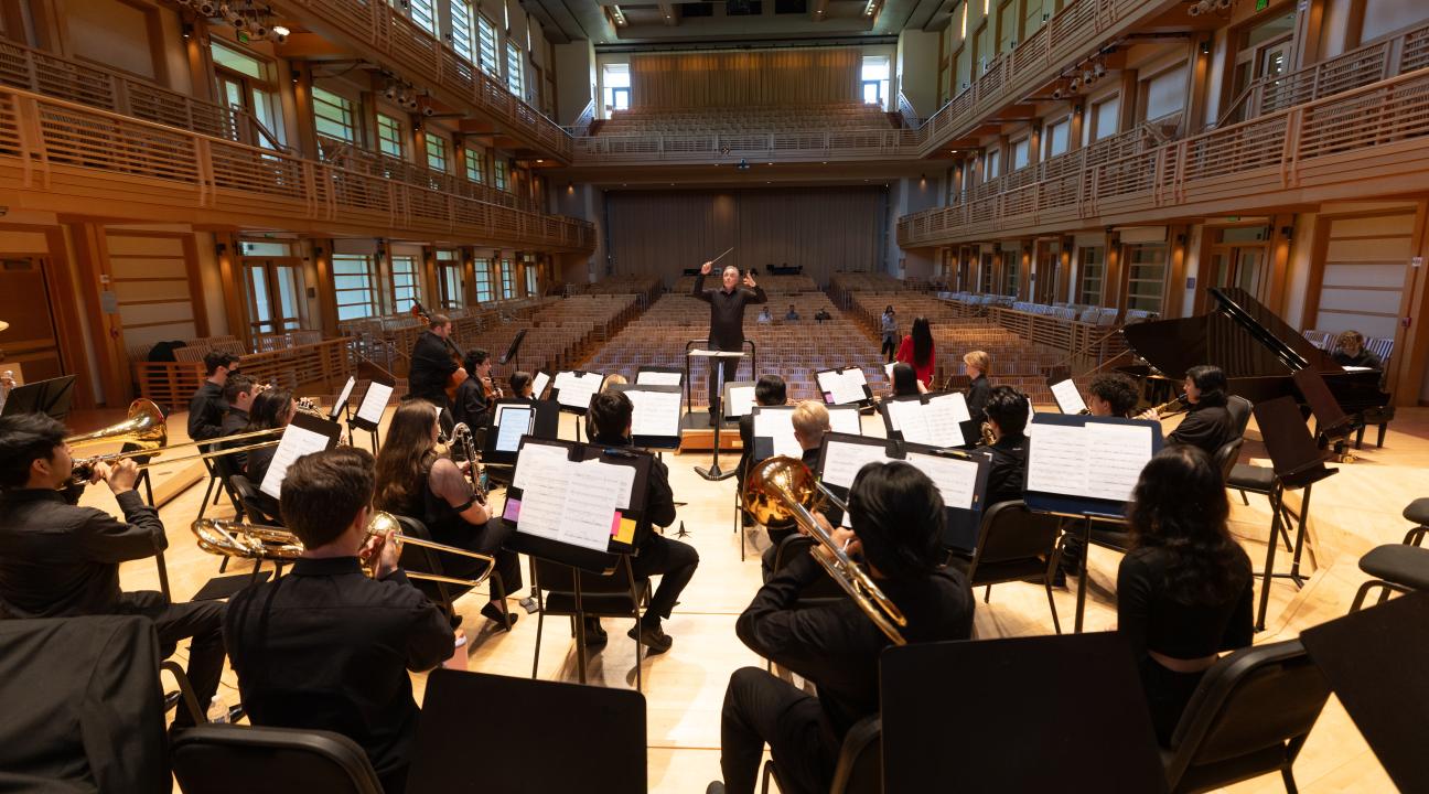 Group of students playing instruments in Weill Hall with a professor conducting