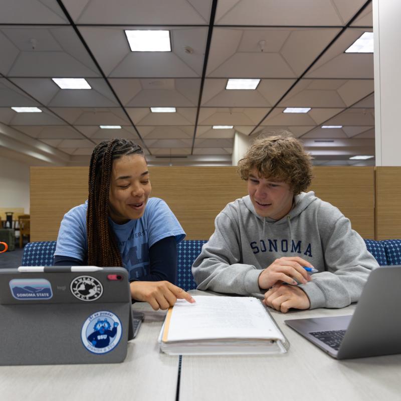 Two students working together and looking at notes in a binder