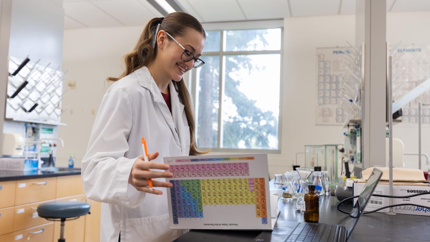 Student in a lab classroom looking down at a binder with periodic table on it