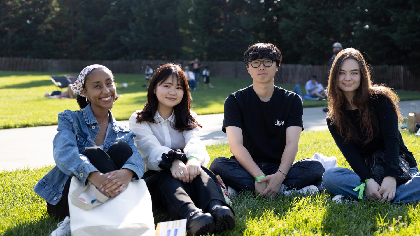 Four students sitting on the lawn smiling