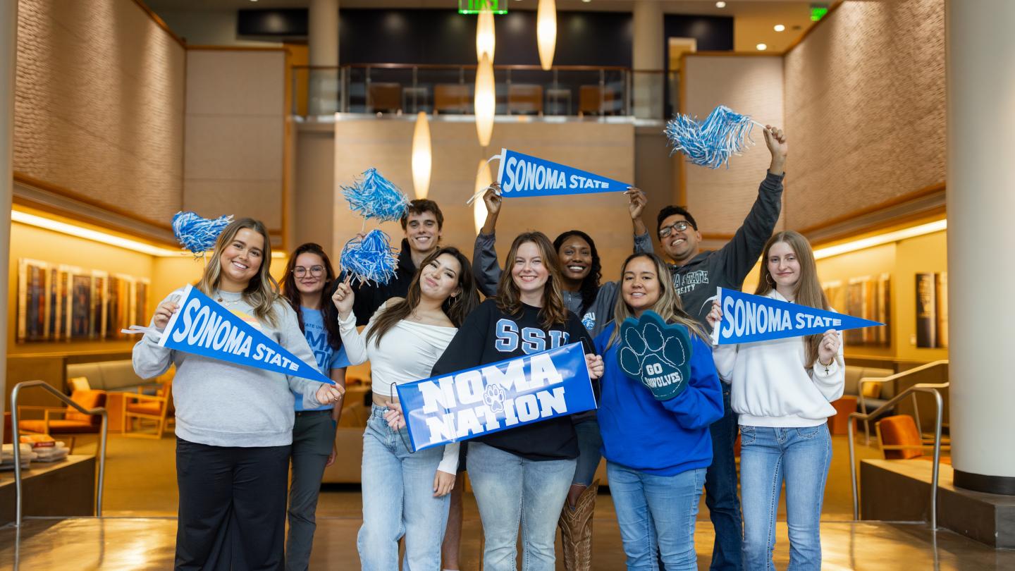 Group of students holding signs with Sonoma State and pom poms in the air