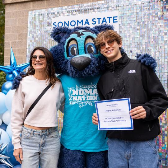 Parent and student smiling and taking a photo with Lobo our mascot