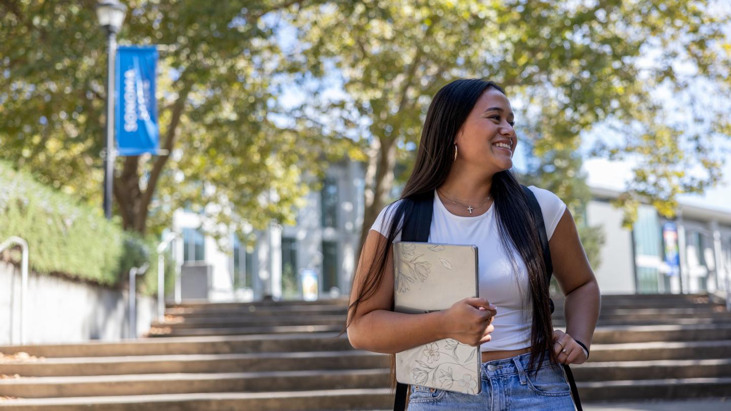 Student holding laptop in her hand and smiling and looking to her left